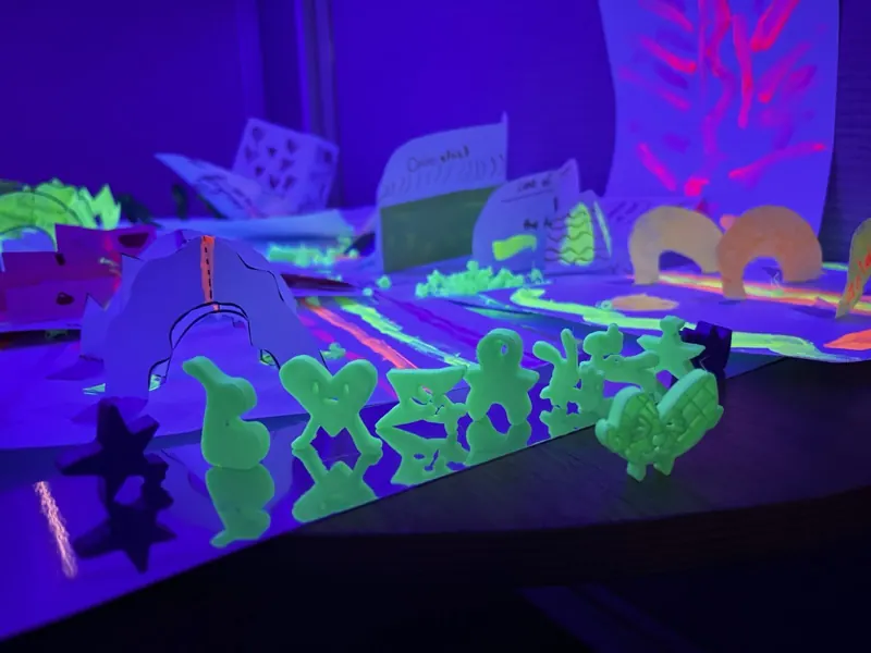 Glow-in-the-dark 3D-printed characters lined up on a pop-up planet