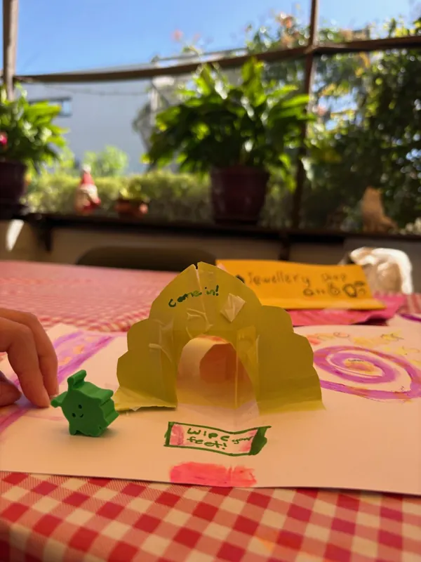 A pop-up paper arch with a small green 3D-printed character