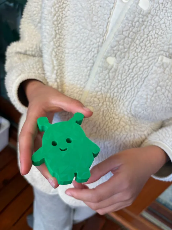 A child holds a small green 3D-printed character
